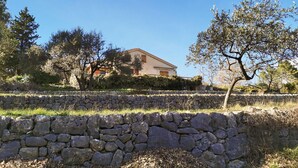Un muro in pietra di fronte a una casa con tetto spiovente e persiane di legno.