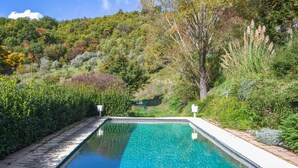Una piscina rectangular con agua azul cristalina, rodeada de abundante vegetación y árboles.