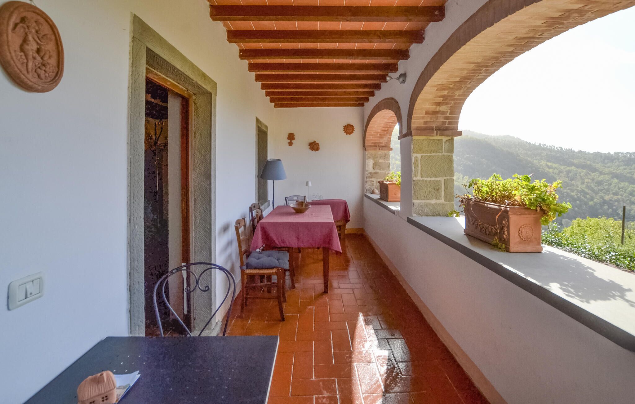 A balcony with a table and chairs, a potted plant, and a view of the countryside.