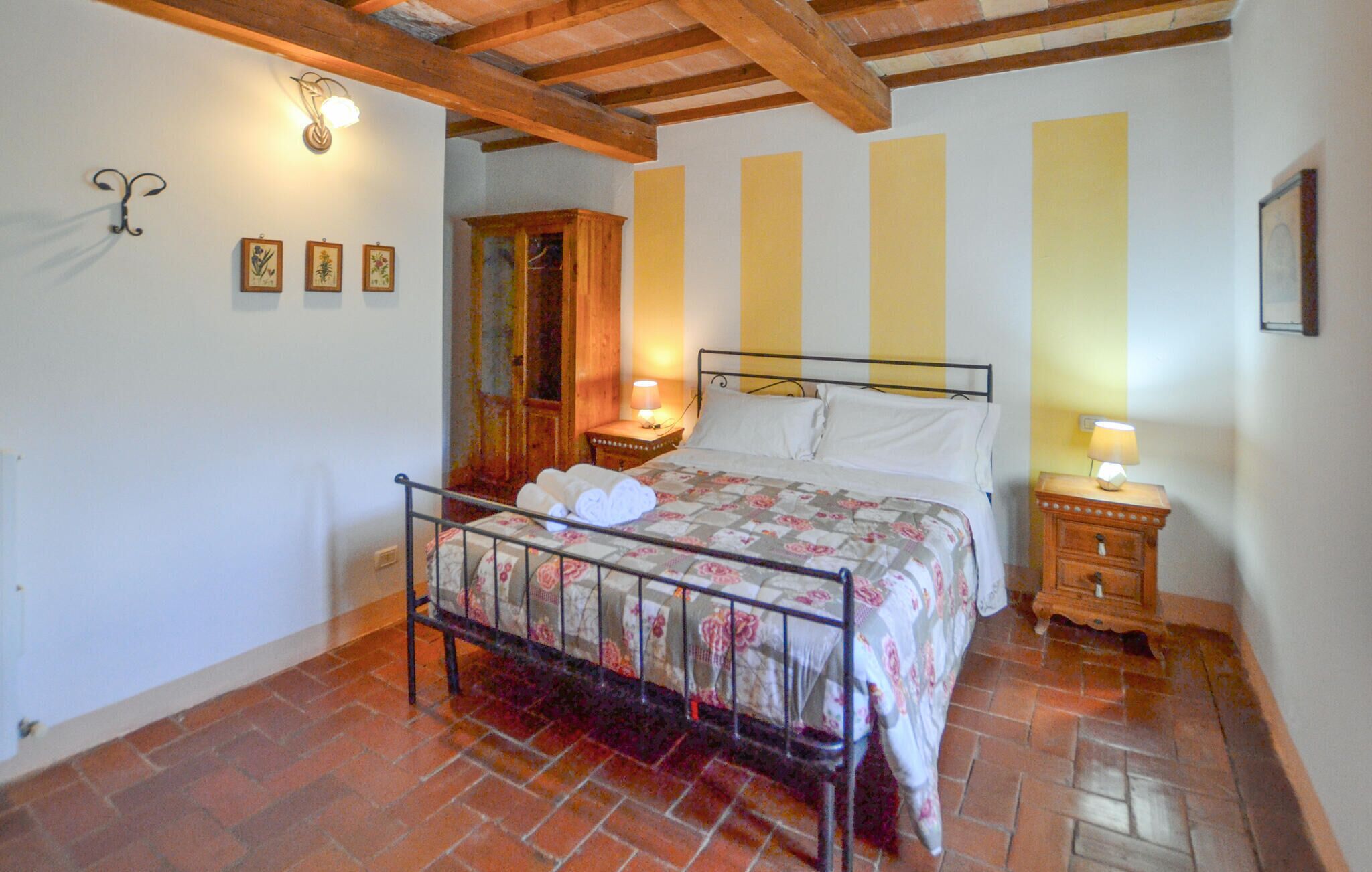 A bedroom with a bed, wooden headboard, a nightstand, a wall-mounted lamp, and a door with a wooden frame.