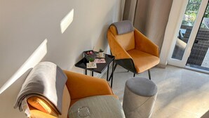 Una sala de estar moderna con dos sillones naranja, una mesita negra con una planta y un otoman gris.