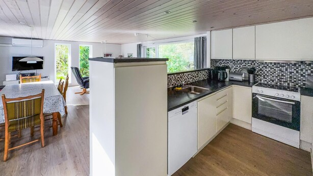 A modern kitchen with white cabinetry, a built-in dishwasher, a stove, and a dining area with a table and chairs. - 3 bedroom stunning home in Tarm (Tarm)