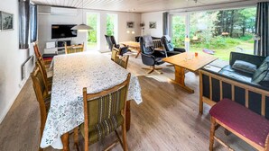 A spacious living area with a wooden floor, a dining table with a floral tablecloth, a sofa, and a TV. - 3 bedroom stunning home in Tarm (Tarm)