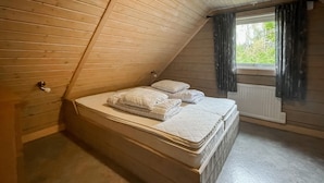 Et lille værelse med skråt tag, en enkeltseng, et vindue med gardiner og en radiator.