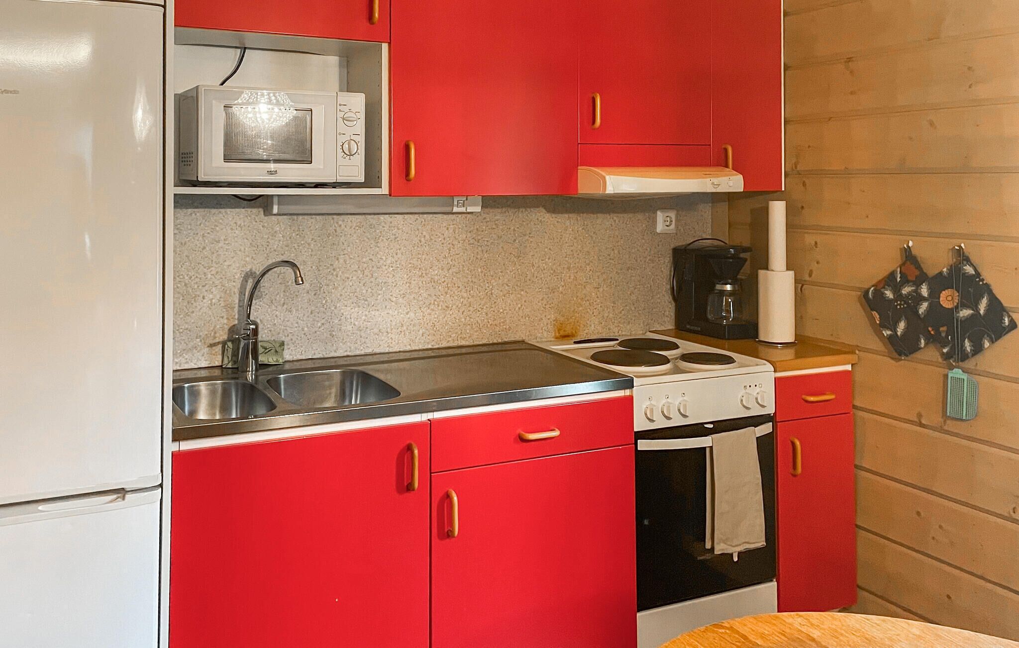A compact kitchen with red cabinets, a white refrigerator, a microwave, a stove, and a sink.