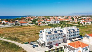 A modern apartment complex with multiple balconies, a parking area, and a view of the sea. - Amazing home in Privlaka with sauna (Privlaka)