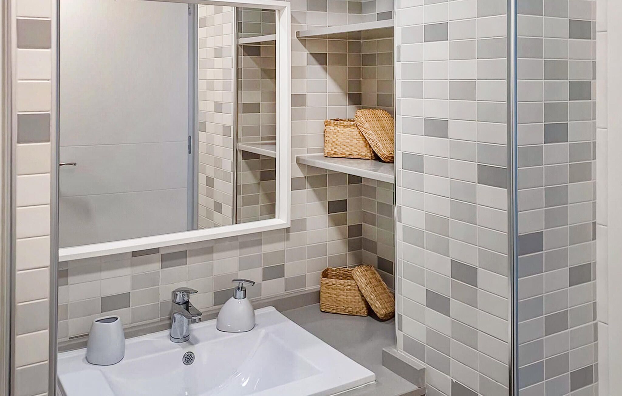 A bathroom with a white sink, two faucets, a mirror, and shelves with baskets.
