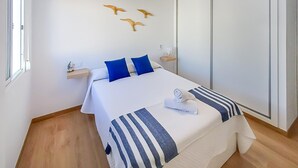 A neatly arranged bedroom with a bed, pillows, a bedside table, a wall-mounted shelf, and a wardrobe. - Amazing apartment in Barbate with WiFi (Barbate)