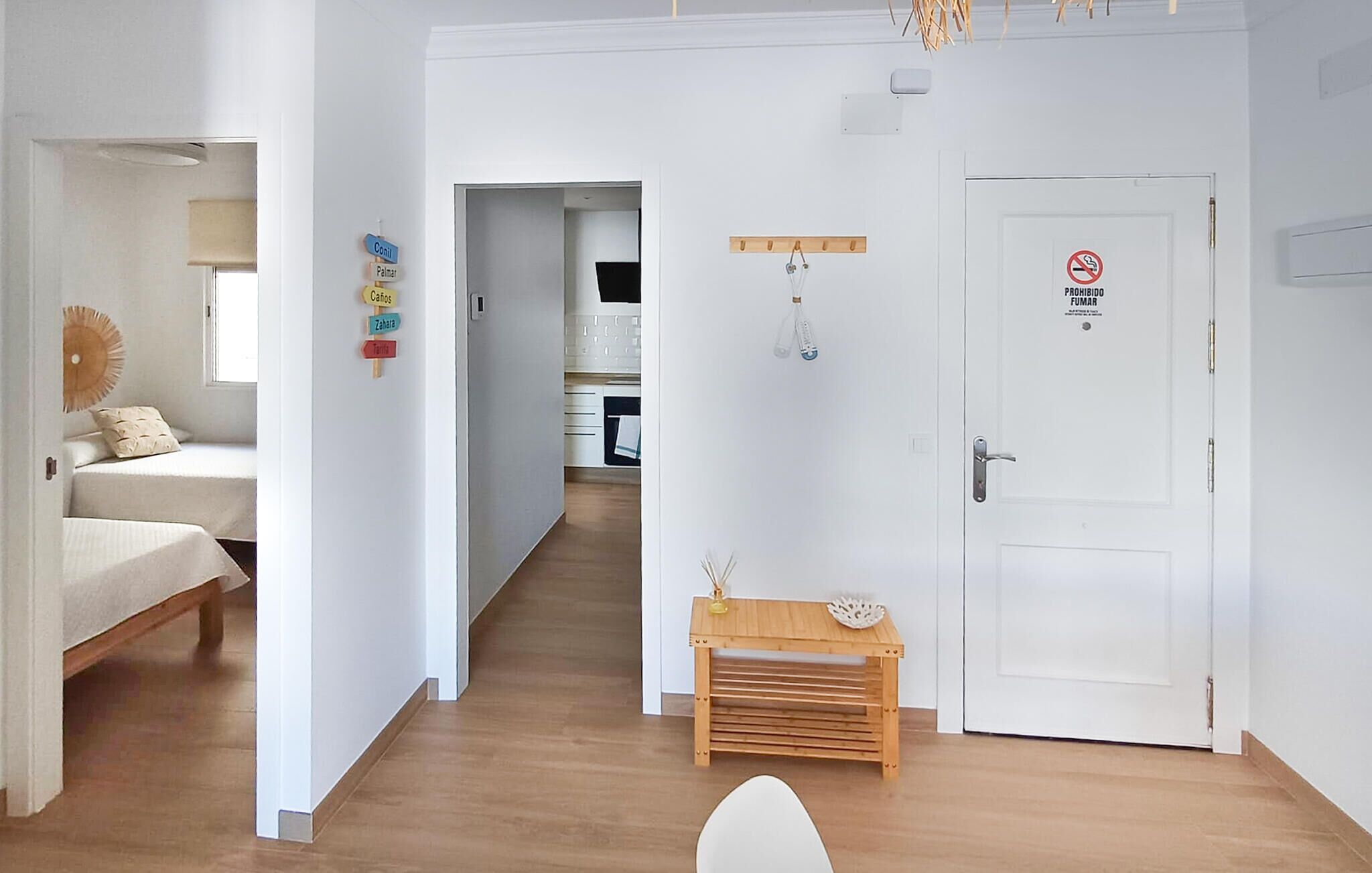A hallway with a bed, a small wooden table, and a door with a no-smoking sign.