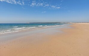 A wide sandy beach with gentle waves, a clear sky, and a distant rocky coastline. - Amazing apartment in Barbate with WiFi (Barbate)
