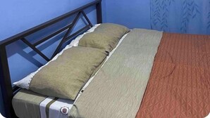Un lit simple avec un cadre en métal, une couvre-lit grise et rouge, et deux oreillers.