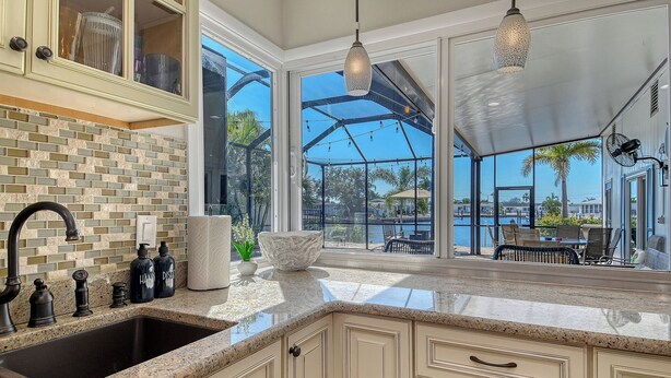 A kitchen with a granite countertop, a sink, and a backsplash. There are cabinets with glass doors and a hanging light fixture. - No Bad Days - Boat Dock, Heated Pool & Hot tub, Beach Gear, 5 Mins to AMI (Bradenton)