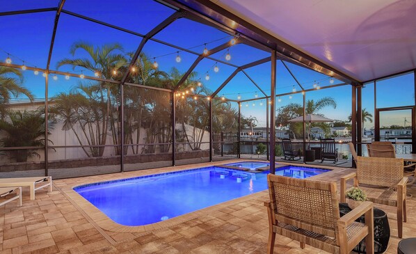 A covered swimming pool area with a clear view of palm trees and a poolside seating area. - No Bad Days - Boat Dock, Heated Pool & Hot tub, Beach Gear, 5 Mins to AMI (Bradenton)