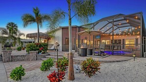 A modern outdoor pool area with a glass enclosure, seating, and a barbecue setup. - No Bad Days - Boat Dock, Heated Pool & Hot tub, Beach Gear, 5 Mins to AMI (Bradenton)
