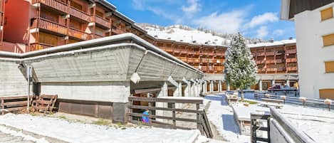 A hotel with multiple balconies, a snow-covered ground, and a view of a mountain.
