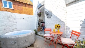 Une petite terrasse extérieure avec un jacuzzi, une table et des chaises, et un mur blanc.