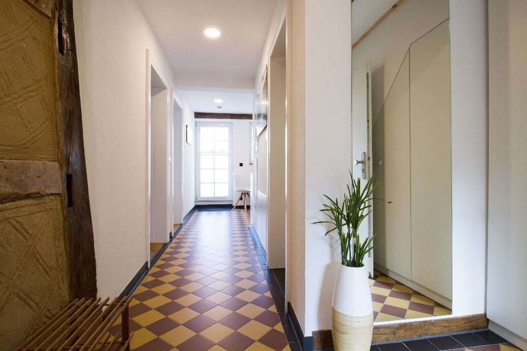 A hallway with a checkered floor, a potted plant, and a door at the end.