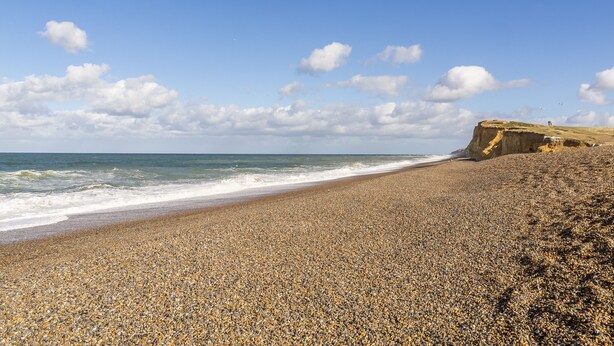 A pebbly beach with a rocky cliff and ocean waves. - Fairstead Cottage, Holt, Norfolk (Holt)