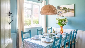 A dining area with a table set for four, chairs, a hanging light fixture, a vase with flowers, and a window with curtains. - Fairstead Cottage, Holt, Norfolk (Holt)