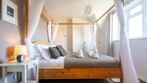 A bedroom with a wooden bed frame, white bedding, a bedside table with a lamp, and a picture on the wall. - Fairstead Cottage, Holt, Norfolk (Holt)