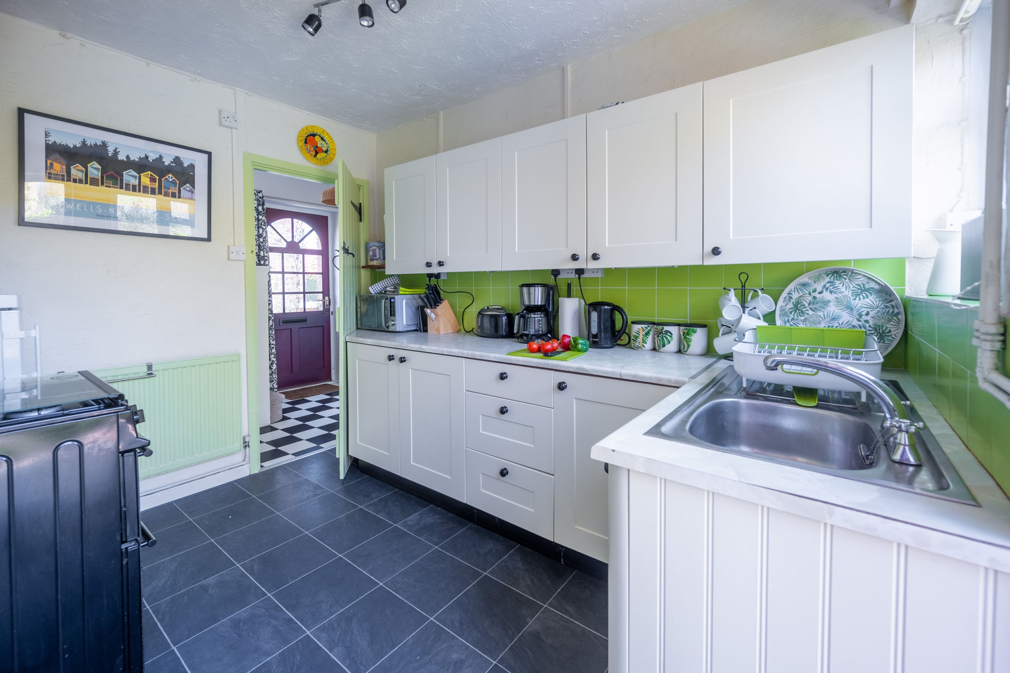 A kitchen with white cabinets, a black and white checkered floor, a green backsplash, and a sink.