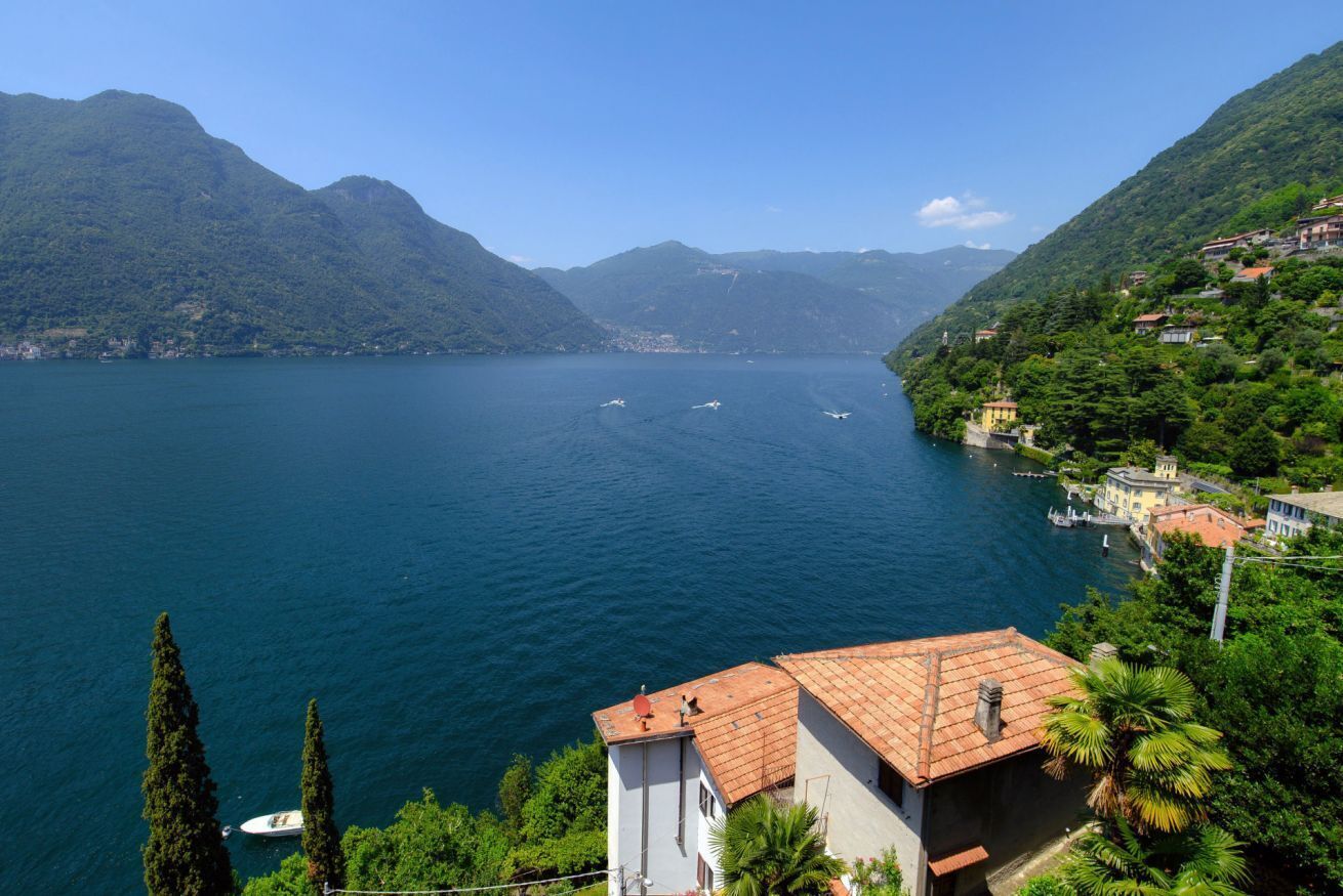 Un lago con barcos, rodeado de montañas y casas con tejados rojos.
