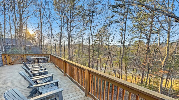 Une terrasse en bois avec des fauteuils Adirondack et une table, donnant sur une zone boisée.