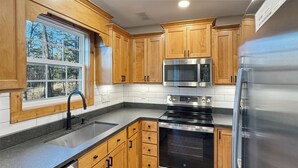 Une cuisine moderne avec des meubles en bois, des appareils électroménagers en acier inoxydable et une fenêtre donnant sur les arbres.