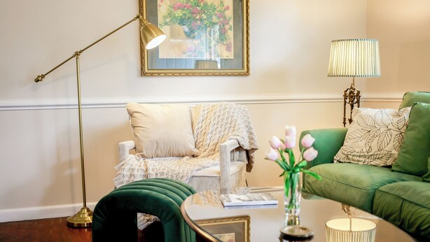 A living room with a green sofa, a white armchair, a green ottoman, a coffee table, and two floor lamps. - Adorable pet-friendly fenced home in Hampton! Welcome to Redheart Cottage <3 (Hampton)