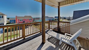 Une terrasse en bois avec une balustrade, une chaise blanche et une vue sur des maisons colorées de l’autre côté de la rue.