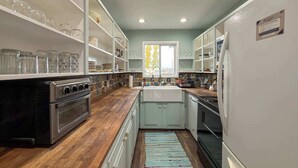 A kitchen with wooden countertops, white cabinets, and a tiled backsplash.