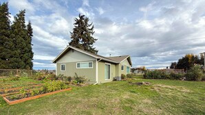 A single-story house with a sloped roof, a front porch, and a small garden area with raised beds.