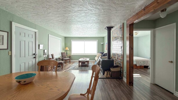 A spacious living room with a wooden dining table, comfortable seating, a fireplace, and a large window providing natural light.