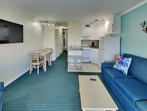 A compact living space with a dining area, kitchenette, and a blue sofa with a colorful pillow. - Casa Del Mar 133 | Private Balcony, Partial Gulf Views (Galveston)