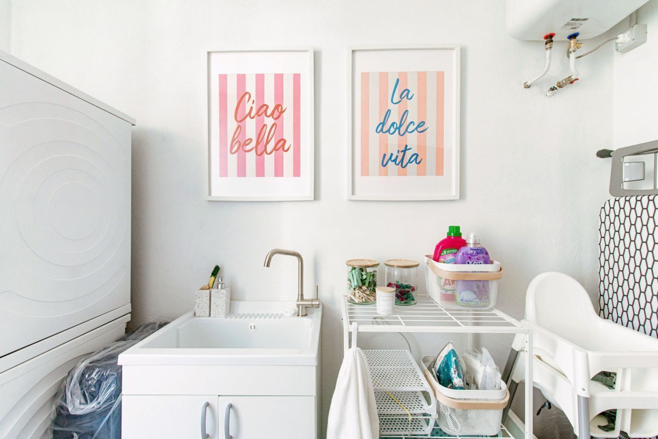 A white bathroom with a sink, a baby changing station, and two framed signs on the wall.