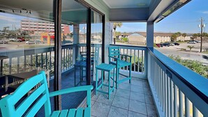 Un balcon avec des chaises et une table de couleur turquoise, une porte vitrée donnant sur l’extérieur et une vue sur une rue et des immeubles.