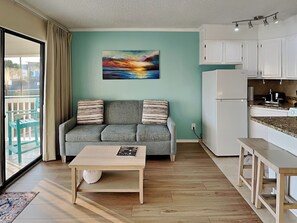 Ein Wohnzimmer mit grauem Sofa, einem Holztisch und einem Gemälde vom Sonnenuntergang.