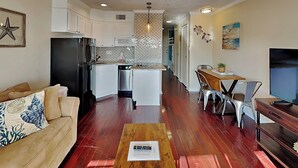 A modern kitchen with white cabinets, a black refrigerator, and a microwave. There is a dining area with a wooden table and metal chairs. - Casa Del Mar 374 | Partial Gulf Views, Pool Access (Galveston)