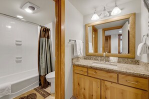 A bathroom with a bathtub, toilet, vanity with a mirror, and a shower curtain. - Spacious 4-Bedroom in Keystone-Walk to lifts! (Keystone)