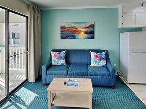 Ein modernes Wohnzimmer mit einem blauen Sofa, einem Couchtisch und einem Gemälde eines Sonnenuntergangs.