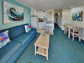 A compact living space with a sofa, a small table, a kitchenette, and a dining area. - Casa Del Mar 258 | Private Balcony, Gulf Views (Galveston)