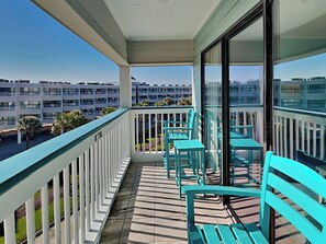 Een balkon met turquoise stoelen en uitzicht op een meerlaags gebouw.