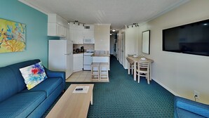 Un espacio habitable compacto con kitchenette, comedor y televisor montado en la pared.