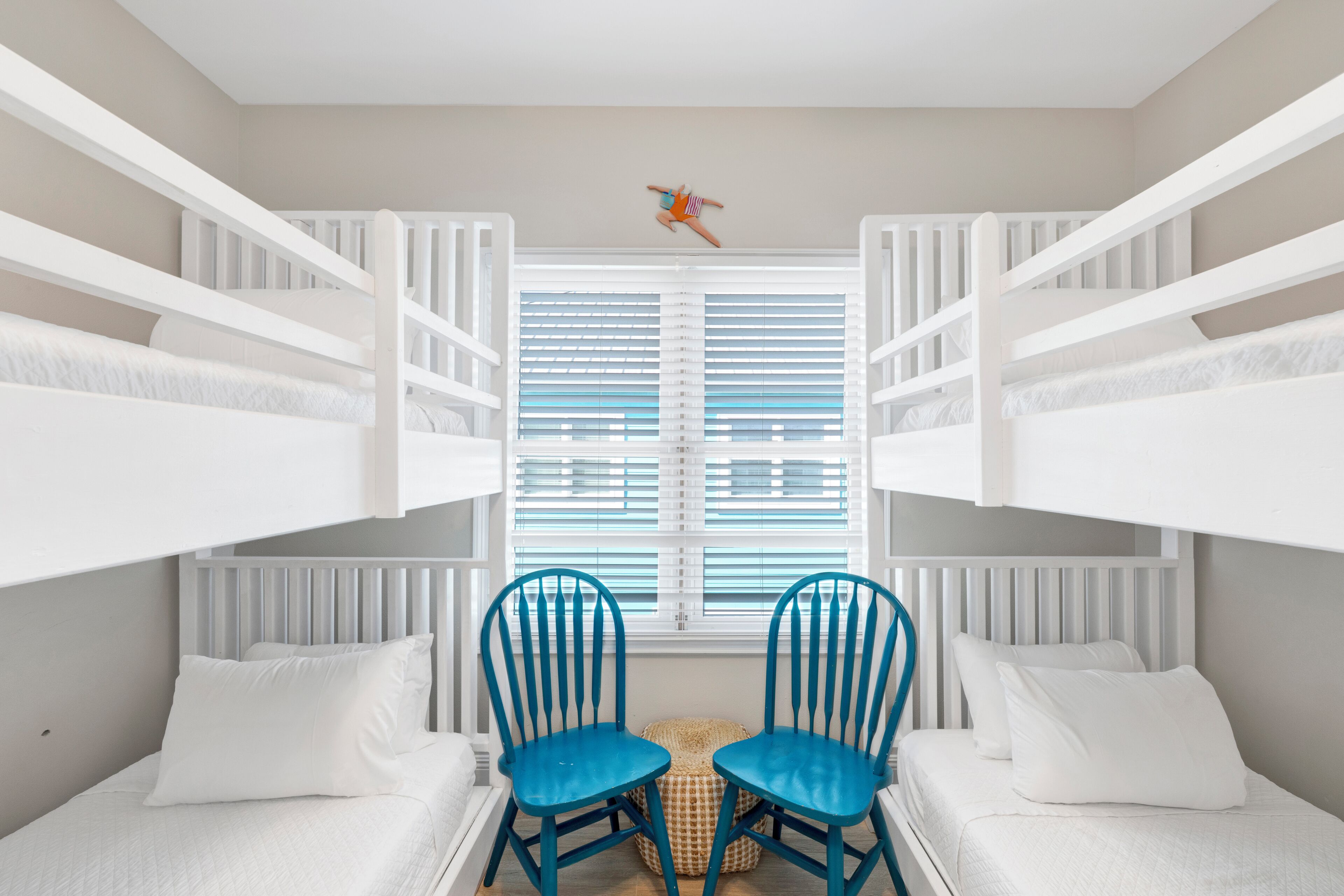 A room with bunk beds, two blue chairs, a window with blinds, and a small decorative item on the ceiling.