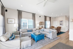 A spacious living room with a sectional sofa, a blue coffee table, and a dining area with a table and chairs. - Gulf-Front Duplex | Pet Friendly | Pools and Pier Access (Fort Morgan)
