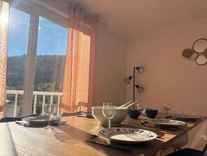 Ein Esstisch ist gedeckt mit Tellern, Schüsseln und Gläsern, mit Blick auf eine grüne Umgebung.