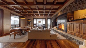 A spacious living room with a fireplace, wooden beams, and a stone accent wall. - Cozy See Forever Condo by InvitedHome | Balcony, Walk to Hike and Festivals (Mountain Village)