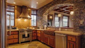 A kitchen with a stone wall, wooden cabinets, a stainless steel stove, and a dishwasher. - Cozy See Forever Condo by InvitedHome | Balcony, Walk to Hike and Festivals (Mountain Village)