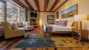 A spacious room with a large bed, two sofas, a fireplace, and a large window with a mountain view. - See Forever Condo by InvitedHome | Ski Valet, Walk to Ski, Hot Tub, Balcony (Mountain Village)