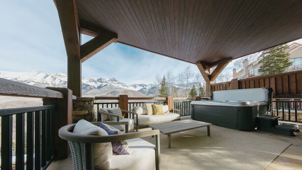 A covered outdoor seating area with a hot tub, sofas, and a view of snow-capped mountains. - See Forever Condo by InvitedHome | Ski Valet, Walk to Ski, Hot Tub, Balcony (Mountain Village)